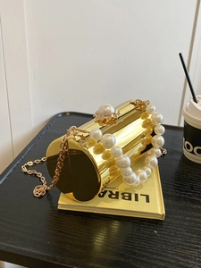 Gros plan d'une pochette cylindrique dorée avec poignée en perles et chaîne métallique