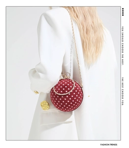 Detail of red polka dot sphere evening bag with gold chain strap on white blazer