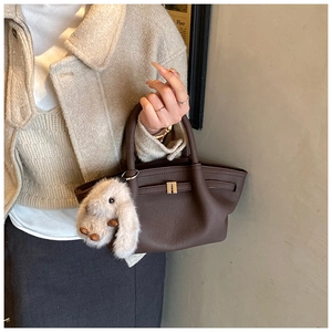Close-up of dark brown lychee textured leather handbag with a plush rabbit charm accessory