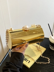 Gros plan d'une pochette cylindrique dorée avec finition miroir et détails en perles