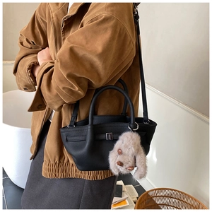 Detail of black pebbled leather bucket bag with metal lock and cute rabbit plush charm