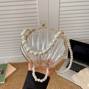 Chic shell shaped acrylic evening bag with pearl handle and golden frame shown on desk