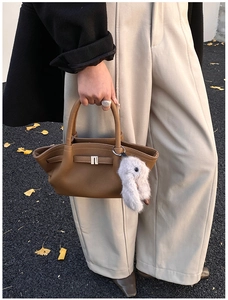 Detail of brown lychee leather handbag featuring a cute plush bunny charm and buckle strap