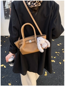 Brown leather bucket bag with white plush rabbit charm on a street style background