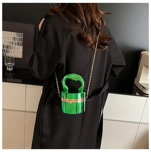 Détail du sac cylindrique vert émeraude avec poignée ondulée et bandoulière dorée