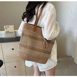 Détail du sac cabas en paille tissée avec anses en cuir marron et décoration à pompons
