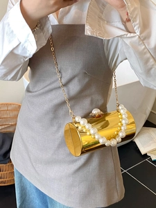 Détail d'un sac de soirée cylindrique doré avec poignée en perles et chaîne fine