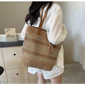 Détail d'un grand sac de plage en paille tressée avec poignées en cuir et pompon