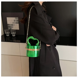 Detail view of a bright green cylinder mirror bag with a gold chain on a black coat