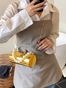 Détail du sac de soirée cylindrique doré avec de grandes perles et une chaîne en métal