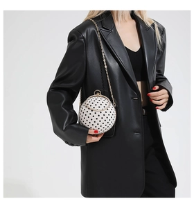 Detailed view of spherical evening clutch with black polka dots and gold ring handle