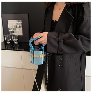 Gros plan du sac cylindre bleu métallisé avec chaîne dorée et poignée incurvée