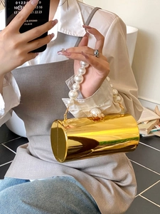 Détail d'un sac de soirée cylindrique doré doté d'une poignée en grosses perles blanches