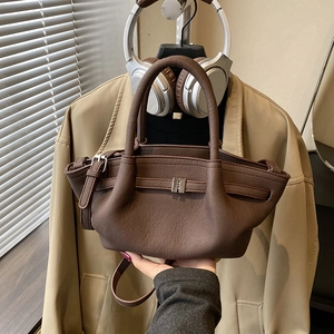 Brown leather crossbody bucket bag with metallic detail on minimalist blazer background