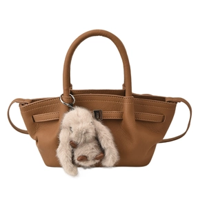 Caramel brown pebbled leather bucket bag with cute plush rabbit charm on white background