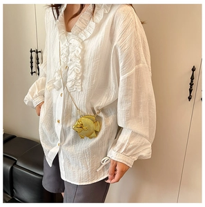 Dettaglio di una borsa da sera dorata a forma di pesce abbinata a una camicia bianca