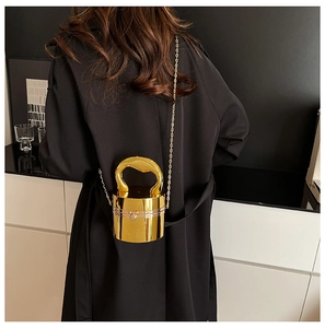 Détail d'un sac de soirée cylindrique doré avec poignée en métal et bandoulière chaîne