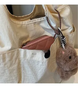 Detail of pink quilted leather coin purse and plush dog charm on a beige tote bag