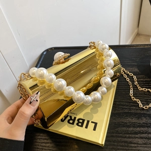 Détail d'une pochette de soirée cylindrique dorée avec perles et chaîne en métal