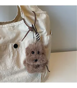 Detailed view of a brown plush dog charm with a silver bone tag on an off-white canvas tote bag