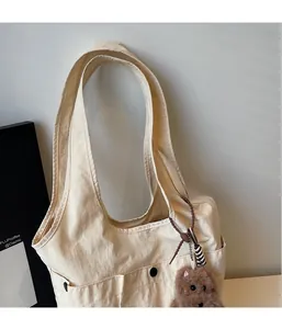 Detail of light beige canvas tote bag with side pocket and cute brown teddy bear charm