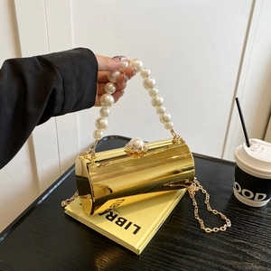 Détail d'une pochette cylindrique dorée avec anse en perles et fermoir en strass sur livre
