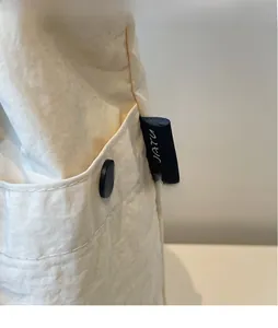 Detail of off-white canvas bucket bag featuring a side pocket with black button and tag