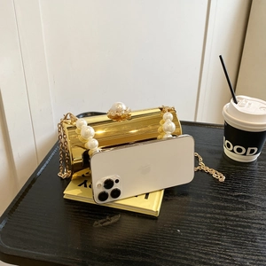 Vue détaillée du sac cylindrique doré avec anse en perles contenant un téléphone