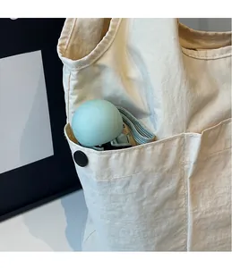 Detail view of the side pocket on a cream tote bag holding a green capsule umbrella