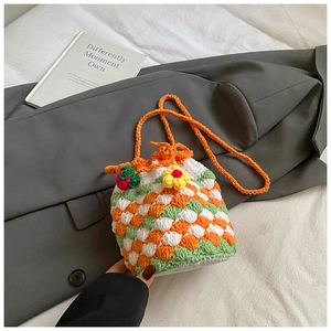Detail of crochet bucket bag with strawberry and flower charms on checkered knit fabric