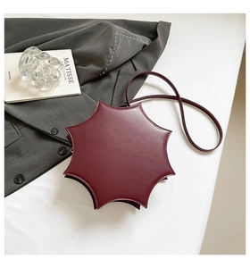 Detailed view of dark red star-shaped crossbody bag on table with artistic props