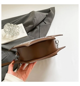 Detail of bat-wing shaped brown crossbody bag with white spider web print and silver hardware