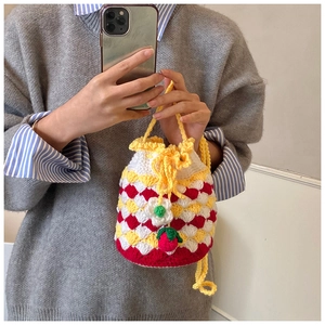 Close-up of handmade crochet bucket bag with red strawberry charm and floral knit details
