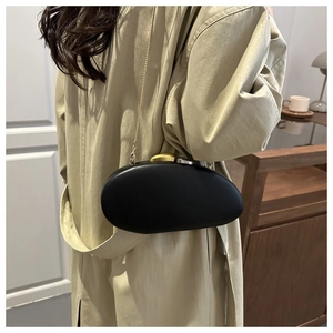 Detail of black pebble-shaped clutch bag with metallic clasp worn on khaki coat