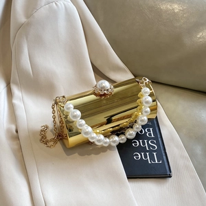Détail d'une pochette cylindrique en métal doré avec boucle perle sur fond de blazer
