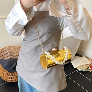 Vue détaillée de la pochette dorée cylindrique avec poignée en perles et bandoulière en chaîne
