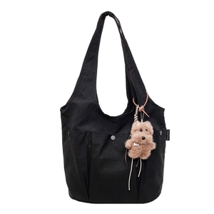 Detail of black canvas tote bag featuring utility pockets and a cute plush puppy charm