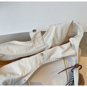 Detail of cream fabric tote bag featuring silver snap button and decorative beaded drawstring