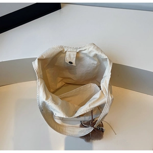 Interior detail of a beige nylon tote bag with snap closure and plush bear pendant