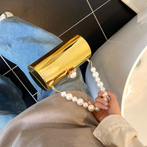 Vue détaillée du sac pochette cylindrique doré avec poignée en perles et fermoir orné