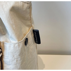Detail of cream canvas bag showing black button pocket and fine stitching quality