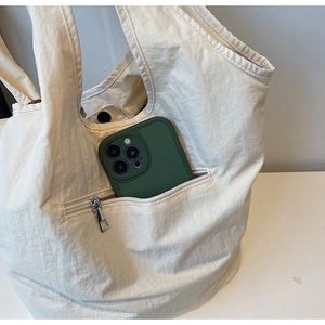 Detail of beige nylon tote bag showing external zipper pocket with a smartphone inside