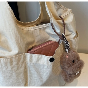 Detail of cute plush animal charm and pink quilted coin purse attached to a canvas bag