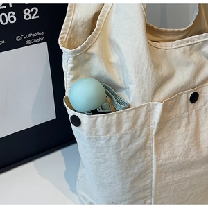 Detail of off-white nylon shoulder bag showing a side pocket with button and blue umbrella