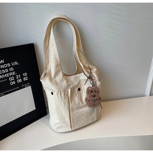 Macro detail of cream tote bag featuring front pockets with snap buttons and bear charm