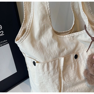 Detail of beige nylon tote bag featuring functional front pockets and a cute plush bear charm