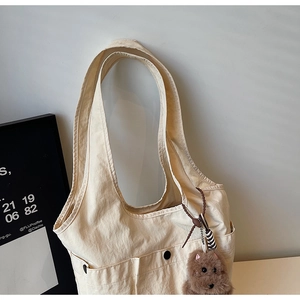 Detail view of cream nylon tote bag with front pockets, snap buttons and plush charm