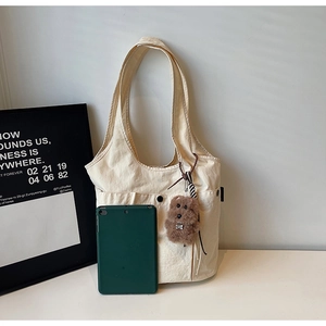 Detail view of off-white canvas tote bag featuring front pocket and cute puppy pendant