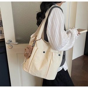 Detail of off-white canvas tote bag with multi-pocket design and cute bear pendant