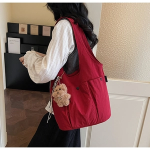 Detail of red canvas tote with multi-pocket design and plush bear charm on shoulder